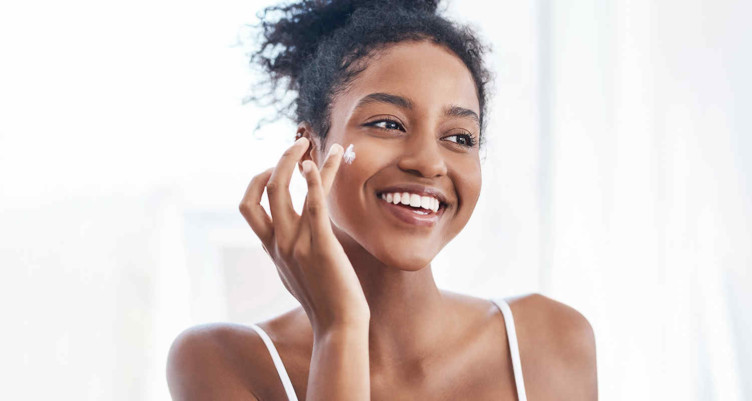 Woman putting face cream on cheek smiling