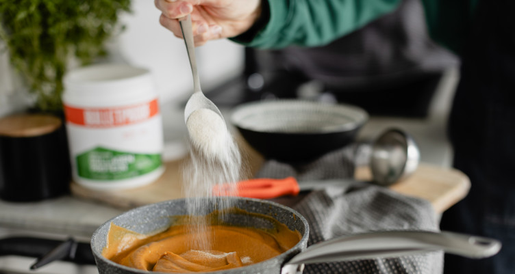 A person adding a scoop of Bulletproof Unflavored Collagen into a pot of soup