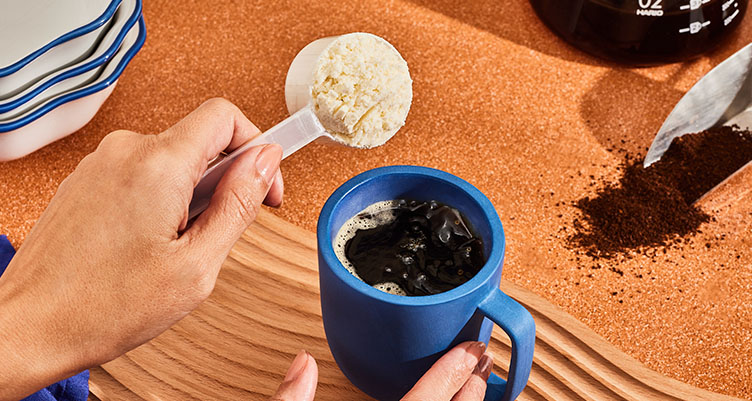 a hand pours a scoop of original bulletproof creamer into a blue mug of coffee