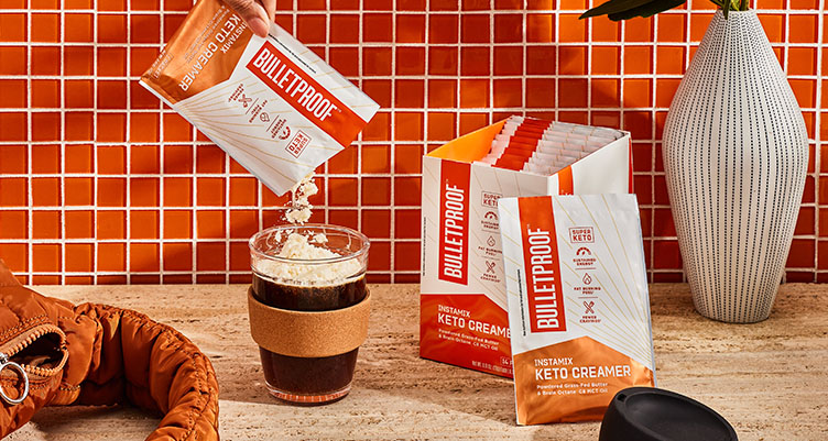 a hand pours a bulletproof instamix on the go original creamer packet into a to-go mug of coffee