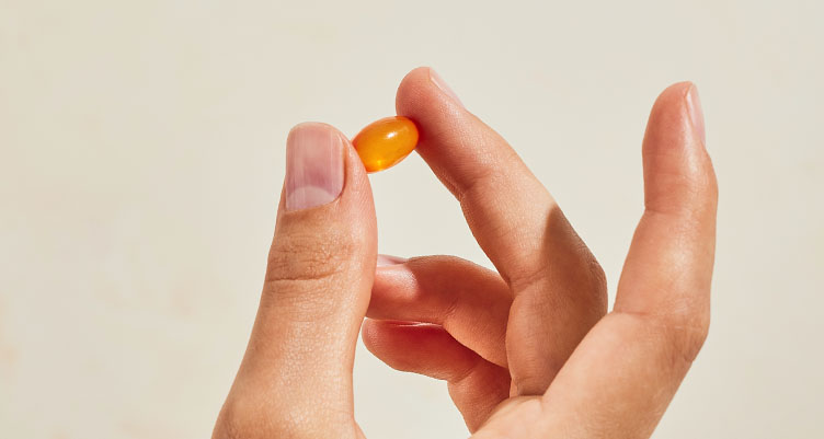 a hand holds an ADK vitamin against a beige background