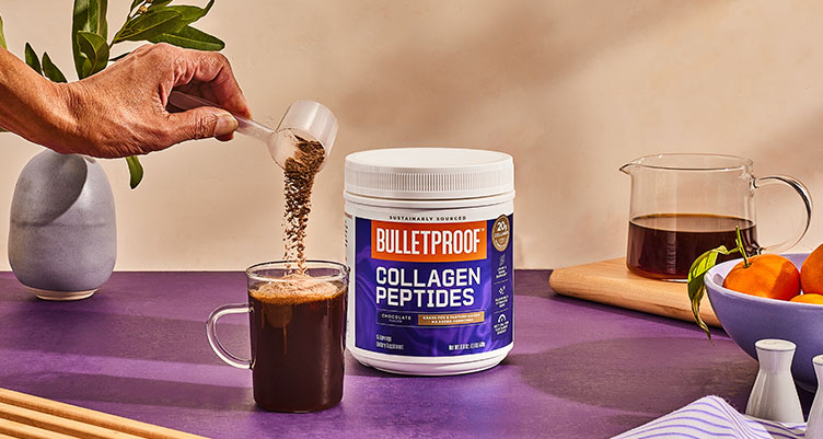 a hand pours a scoop of chocolate collagen peptides into a clear mug of coffee