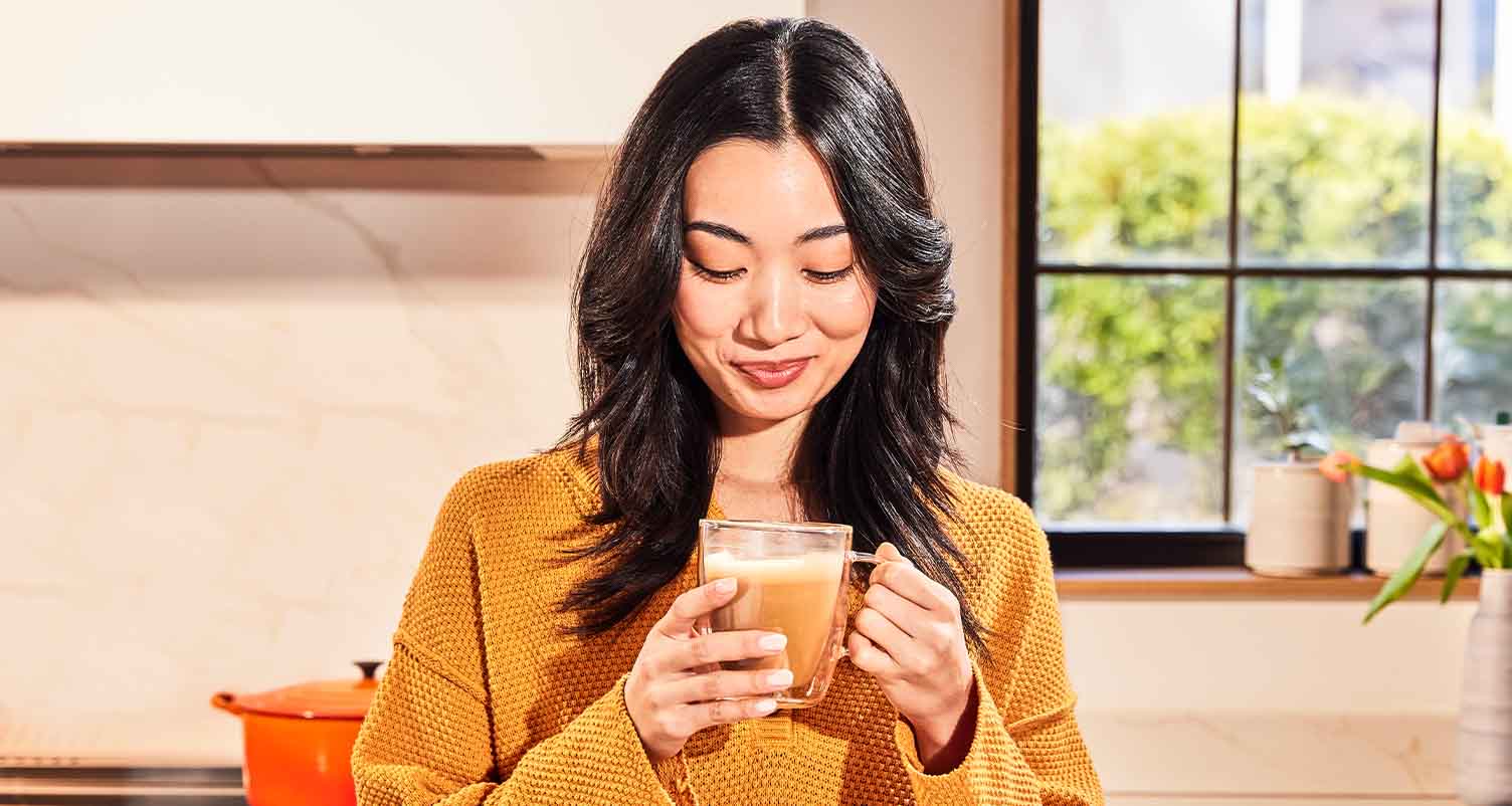 Woman smiling and looking down at a cup of coffee in her hands.