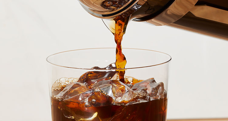a pot of iced coffee pours into a transparent cup over ice