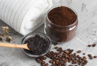 Jar of coffee grounds next to rolled up white towel and coffee scrub mixure