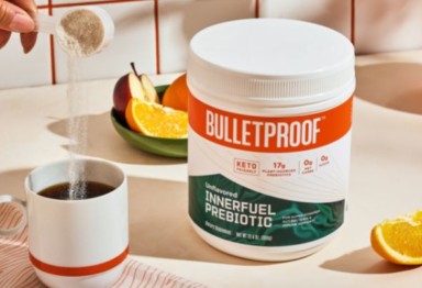Hand scooping Bulletproof Innerfuel Prebiotic into coffee mug next to tub