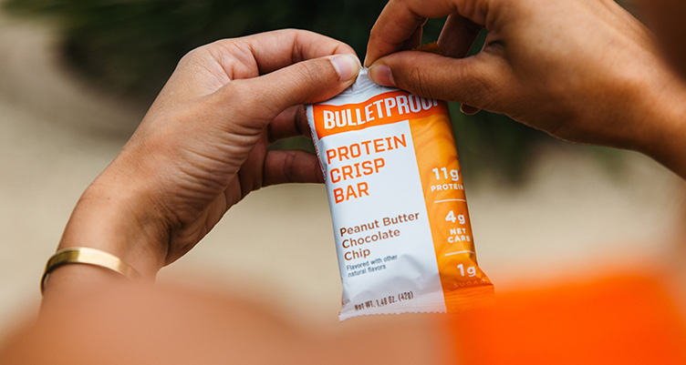 a hand holds a peanut butter chocolate chip crisp bar in packaging close up