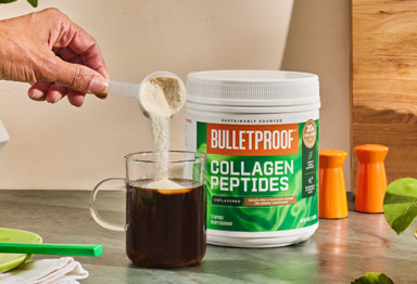 a hand pours a scoop of unflavored collagen peptides into a clear mug of coffee