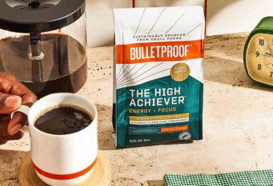 Bulletproof The High Achiever™ coffee bag next to hand holding brewed mug