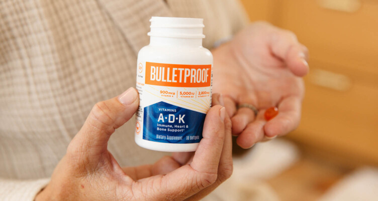 Woman holding Bulletproof A-D-K Vitamins bottle in one hand & the orange capsule in the other hand close to the chest