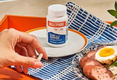 Bottle of Bulletproof Zinc with Copper on plate with hand holding the supplement pill