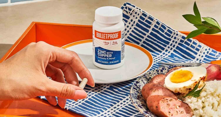 Bottle of Bulletproof Zinc with Copper on plate with hand holding the supplement pill