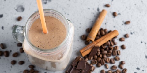 A mason jar of a coffee smoothie with cinnamon sticks