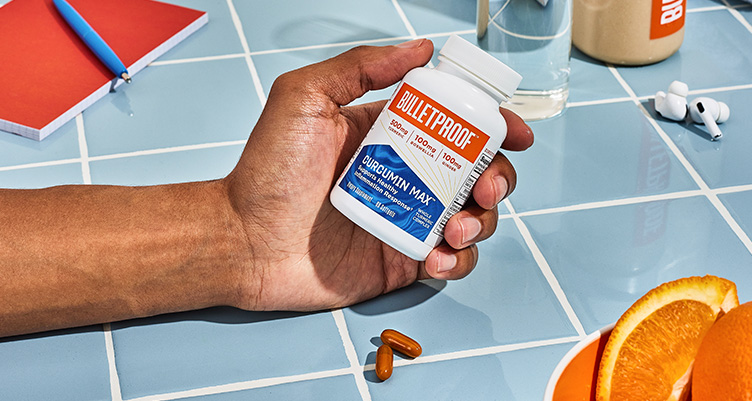 hand holding bottle of Bulletproof Curcumin Max on a blue tiles countertop