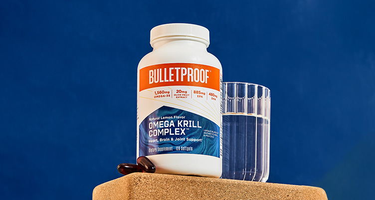a bottle of omega krill, 2 pills, and a glass of water sits on a table with a blue background