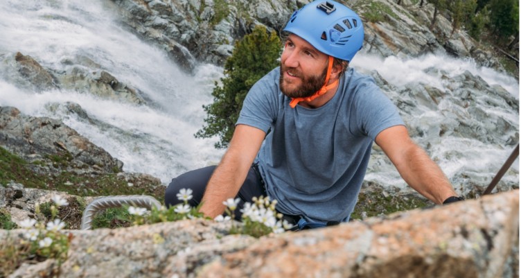 Man climbing rock above waterfall.