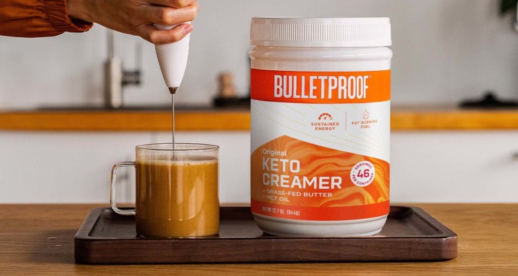 Bulletproof Keto Creamer tub next to a hand frothing a cup of coffee