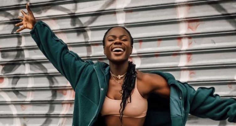 A black woman in a jacket smiling with wide arms
