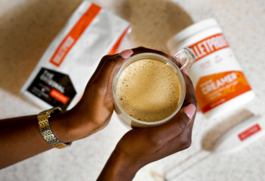 An overhead shot of hands holding a coffee cup and Bulletproof Coffee ingredients