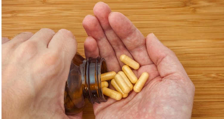 Person pouring bottle of vitamin B complex pills into palm.