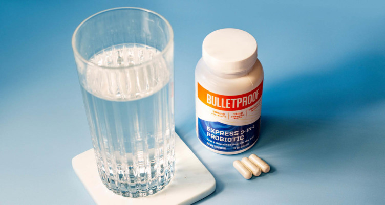 Bulletproof Express 3-in-1 Probiotic next to a full glass of water.