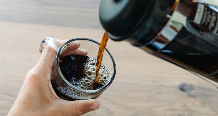 Coffee being poured from a french press into mug