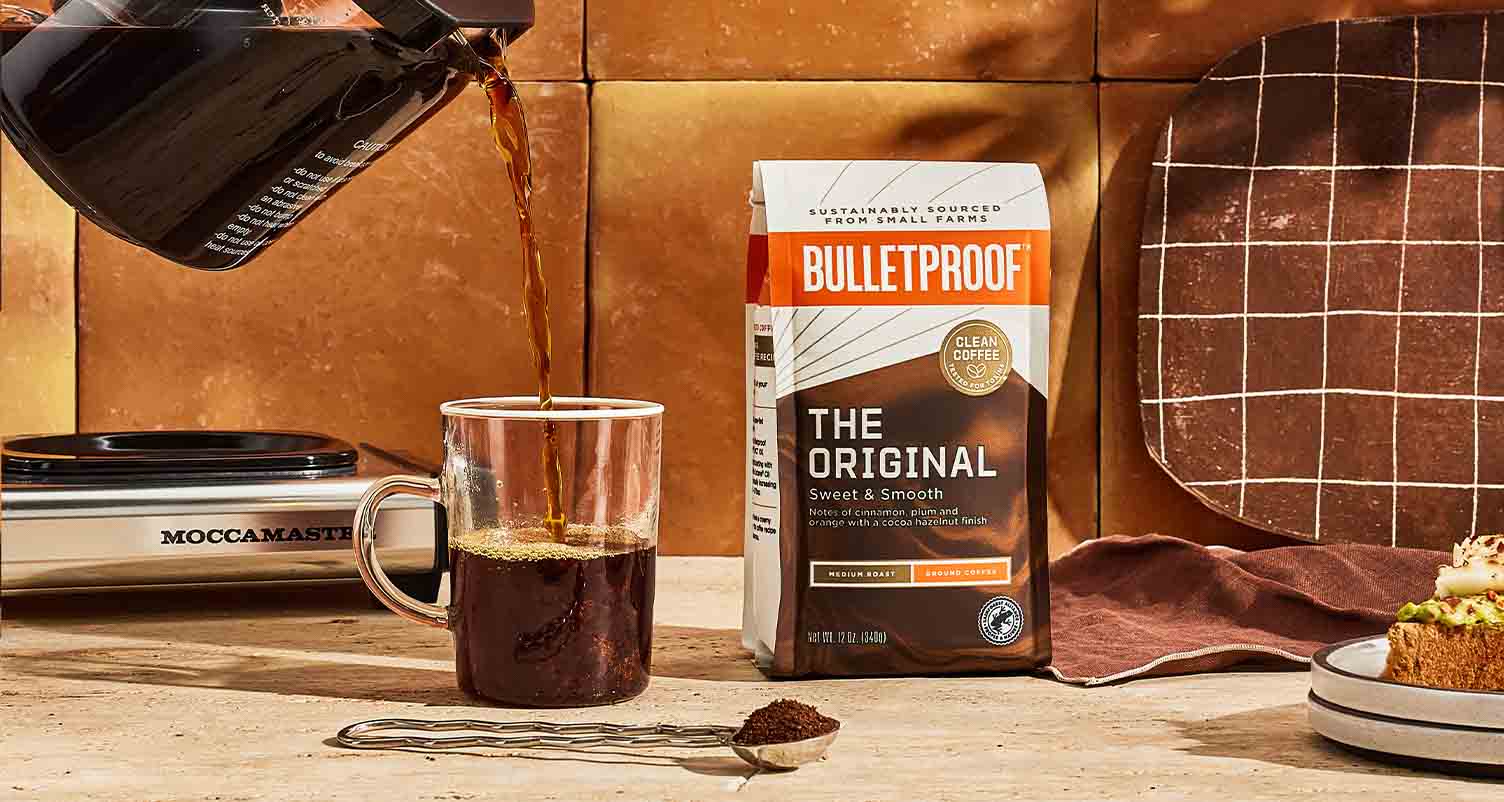 https://www.bulletproof.com/wp-content/uploads/2021/09/coffee-pouring-into-mug-next-to-bag-of-grounds.jpg