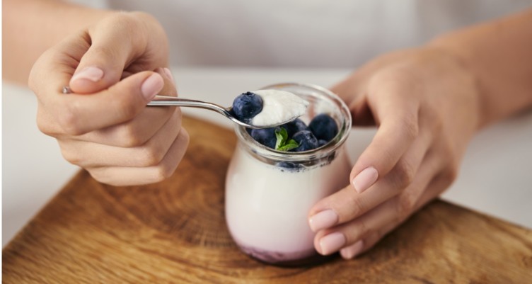 Woman at table with yogurt topped with blueberries.