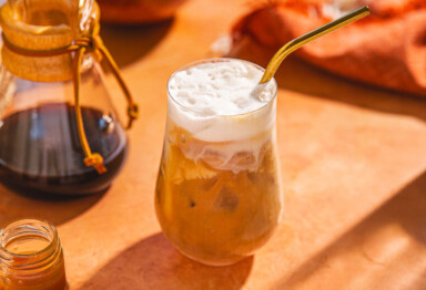 Glass of caramel iced coffee next to chemex and jar of caramel
