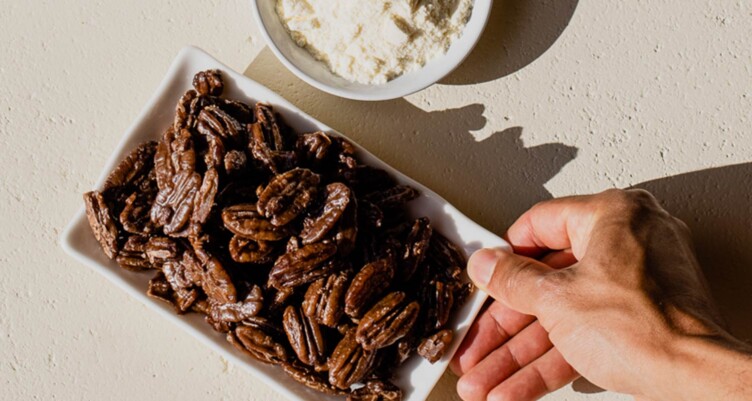 Hand grabbing a plate of candied pecans made with Bulletproof Original Enhanced Creamer.