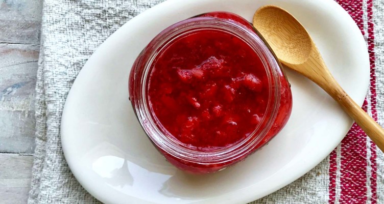 An overhead photo of a jar of jam on a white plate with a wooden spoon