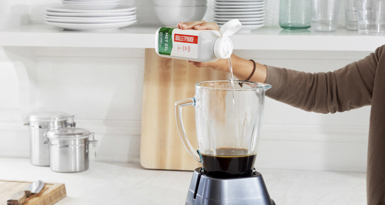 A hand pouring Bulletproof MCT oil into coffee in a blender