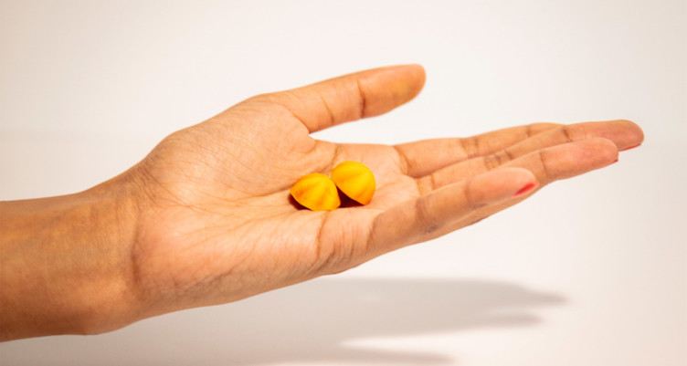 A hand holding two yellow gummy vitamins