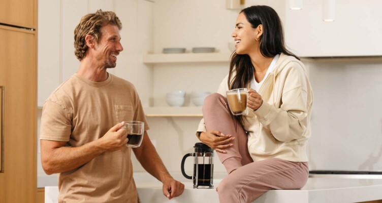 Two people smiling and conversing between one another with coffees in hand