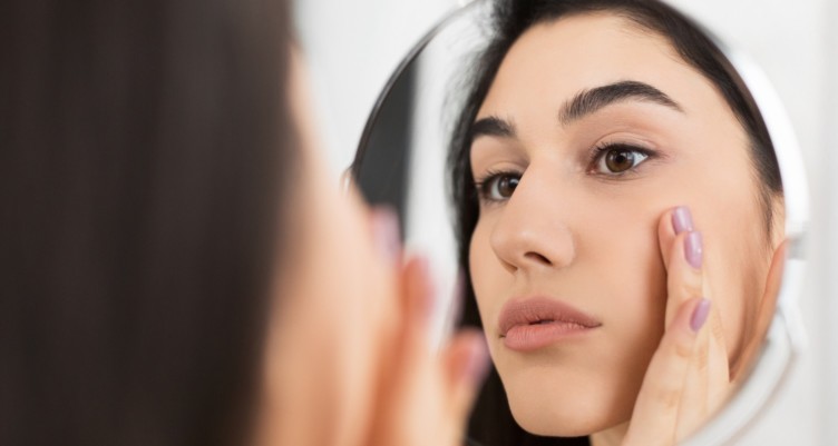 Woman touching face while looking in mirror