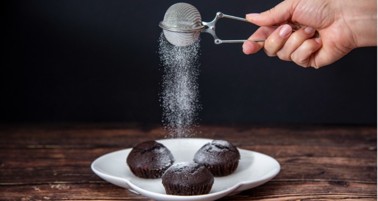 Woman sprinkling icing sugar on chocolate muffins
