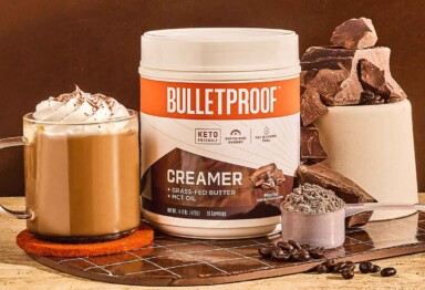 Bulletproof Mocha Creamer tub sitting next to coffee drink and a pile of chocolate chunks and coffee beans