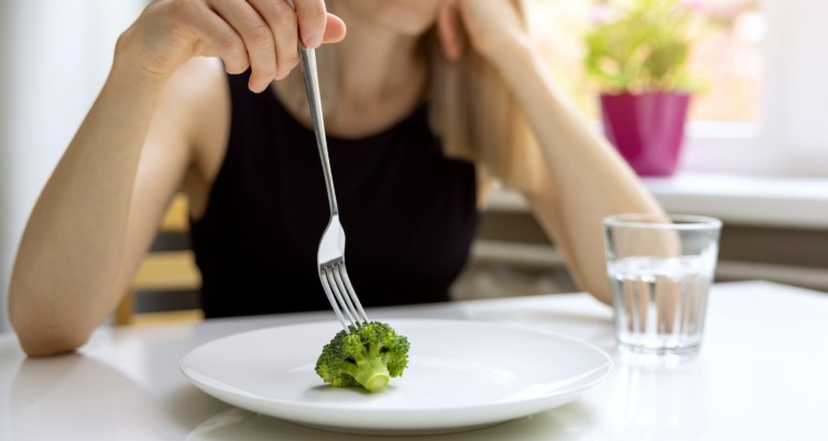 Woman eating a single piece of broccoli off a plate.