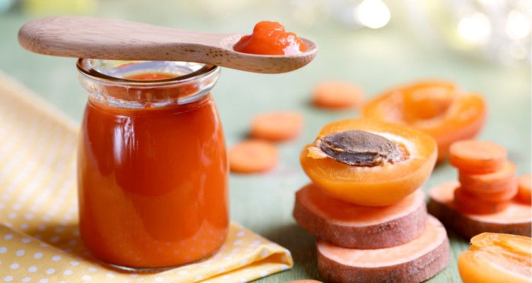 Spoonful of homemade baby food sits on top of a jar of apricot baby food.