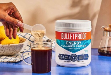 Bulletproof Vanilla Energy Collagen being scooped into a mug of coffee next to tub