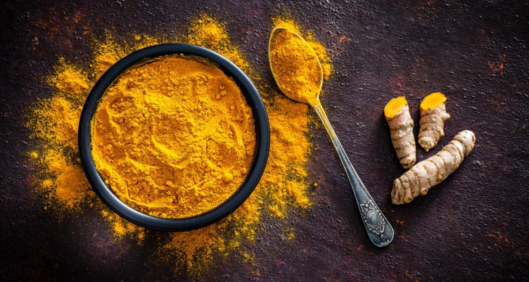 Turmeric roots alongside a bowl and spoon with powdered turmeric.
