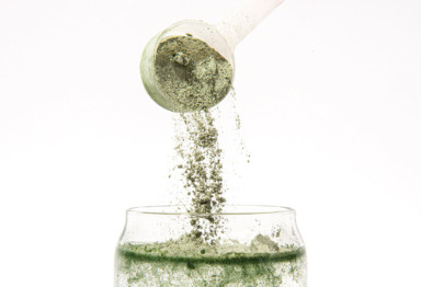 A scoop of Greens powder going into a glass of water