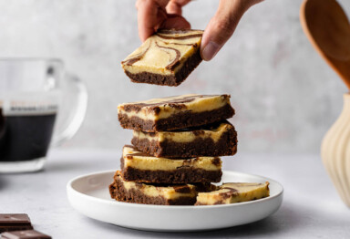 hand grabbing from a stack of keto-friendly cheesecake brownies