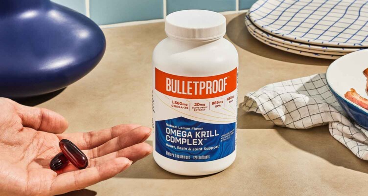 Hand holding Bulletproof Omega Krill Complex supplements next to bottle on counter