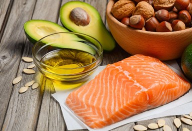 Oil, avocado, a bowl of nuts, salmon and pumpkin seeds on a wooden backdrop
