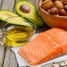 Oil, avocado, a bowl of nuts, salmon and pumpkin seeds on a wooden backdrop