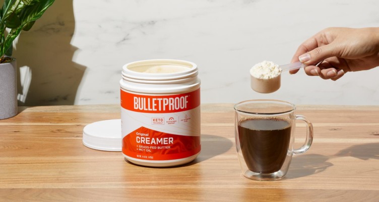 Person putting a scoop of Bulletproof Original Creamer into a cup of coffee.