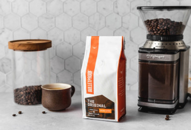 A jar of coffee beans, a cup of coffee, a bag of Bulletproof The Original Coffee and a coffee maker