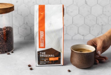 Holding a cup of coffee next to a bag of Bulletproof The Original Coffee Beans