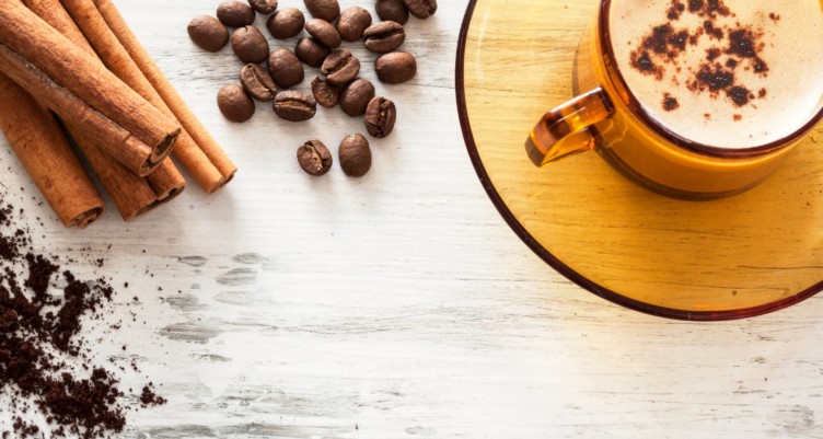 Coffee cup and beans on a wooden table with cinnamon sticks